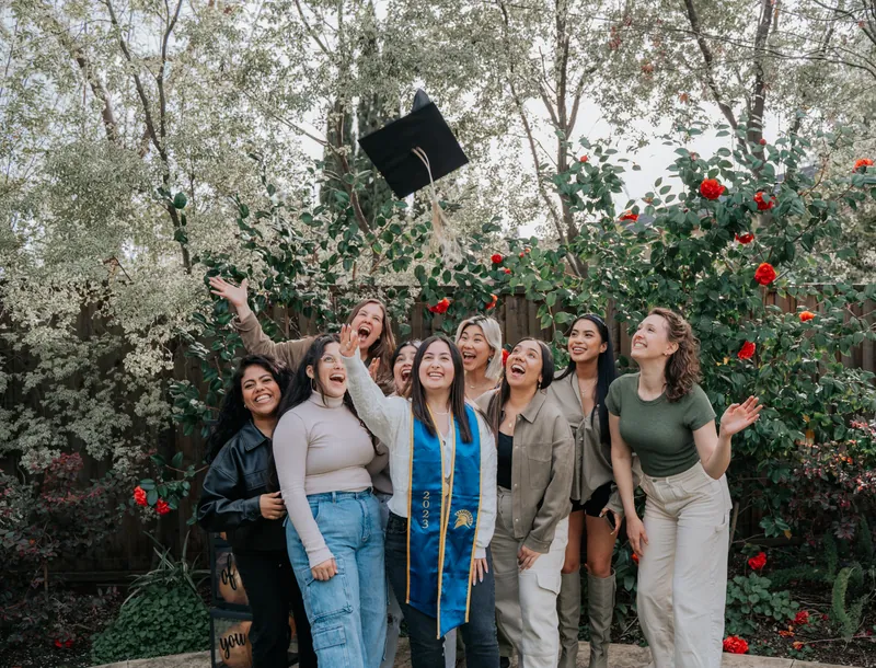 A graduation cap flying over a group of laughing friends