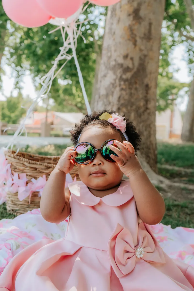 A one-year-old in pink holding up big sunglasses
