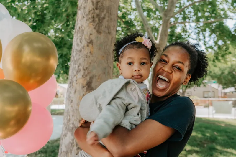 A mom and her one-year-old laughing among pink and gold balloons