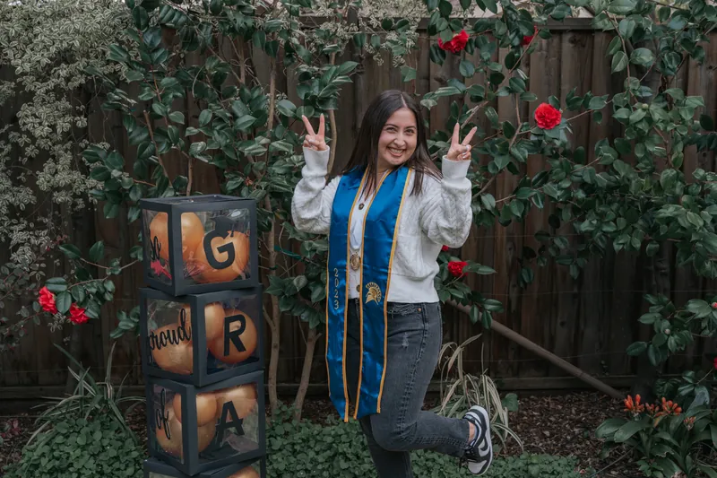 A graduate making peace signs beside GRAD letter blocks