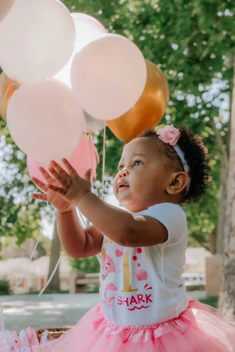 A one-year-old reaching for balloons