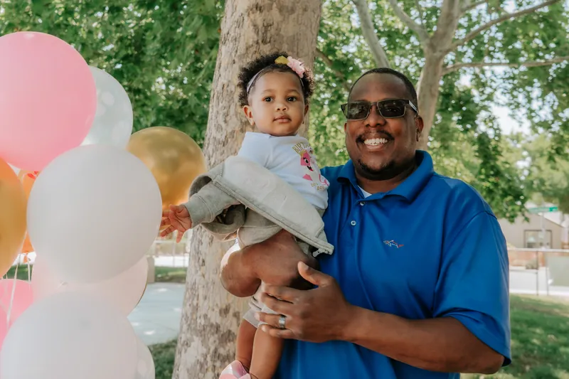 A dad holding his one-year-old beside a bunch of balloons