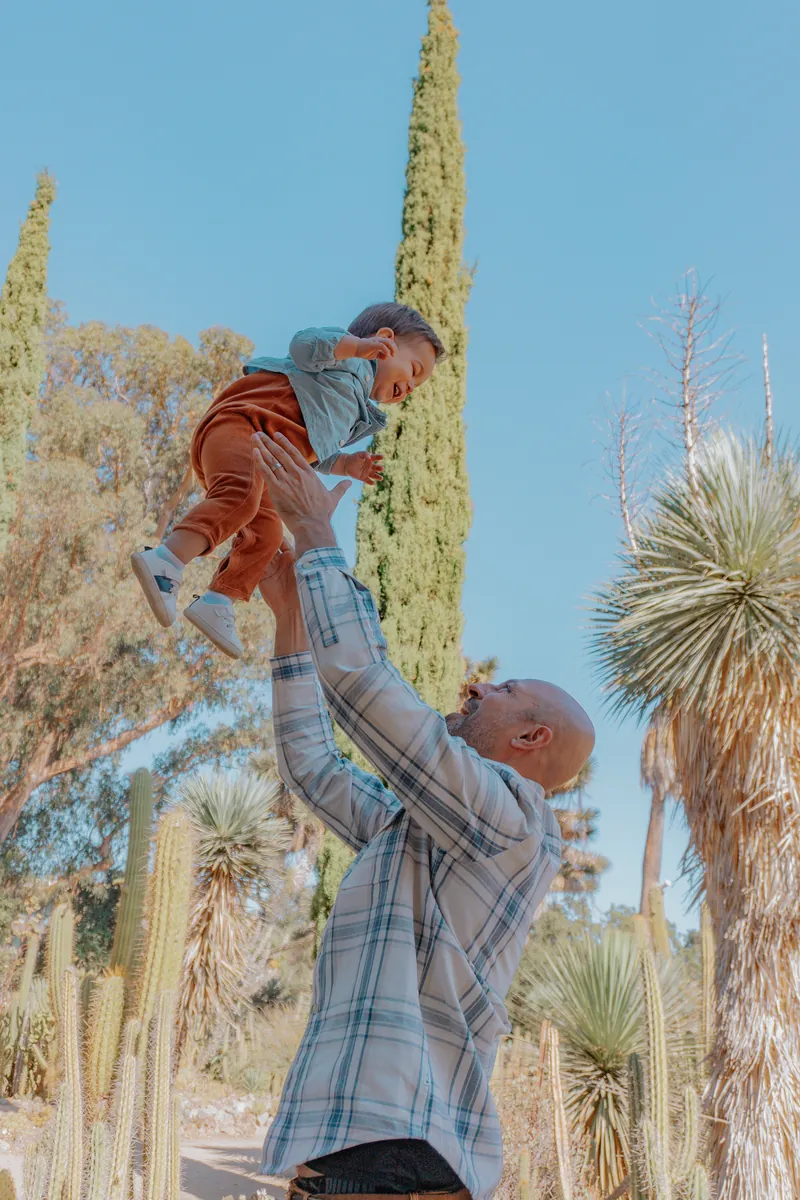 A dad tossing his baby into the air in a desert garden