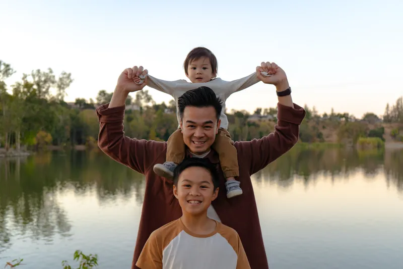 A dad with the baby on his shoulders and his son in front