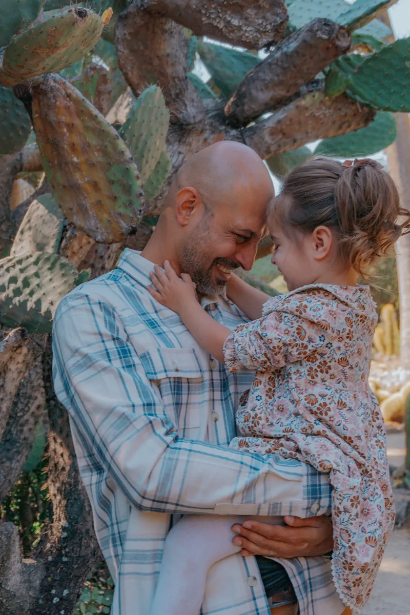 A dad and his daughter, foreheads together, in a cactus garden