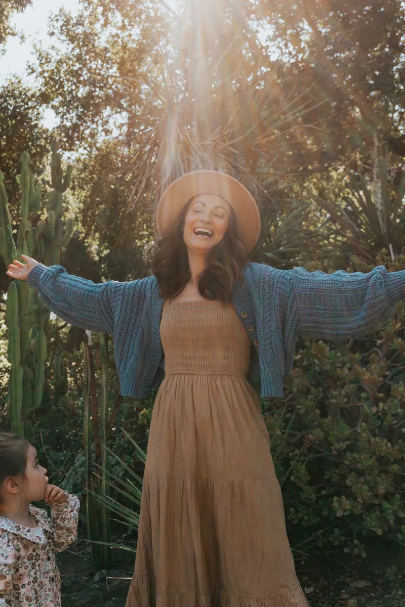 A mom with her arms out in the sun while her daughter watches