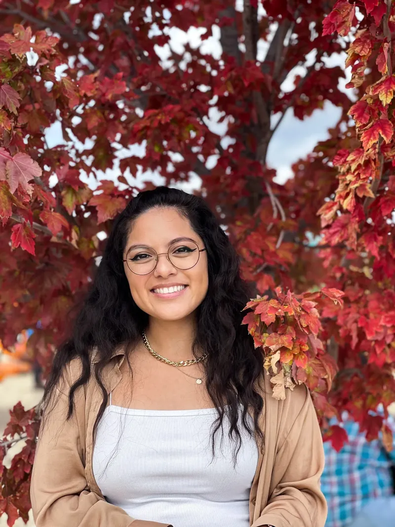 Dianne, the photographer behind Dianne Captures, smiling under a red maple tree