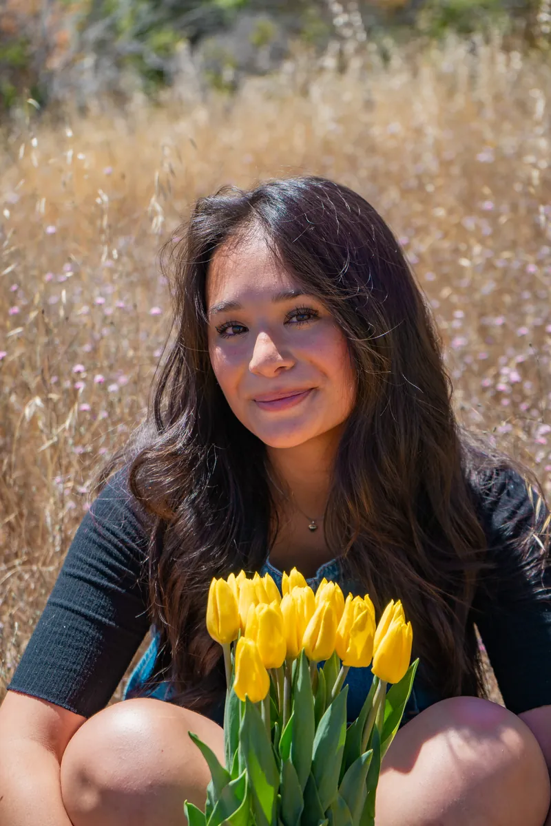 A young woman smiling with a bunch of yellow tulips in a golden field