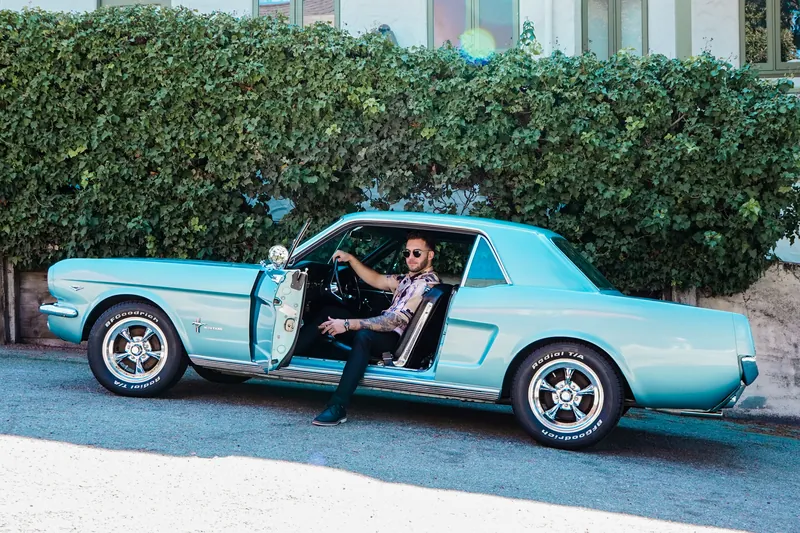A man sitting in a classic turquoise Ford Mustang