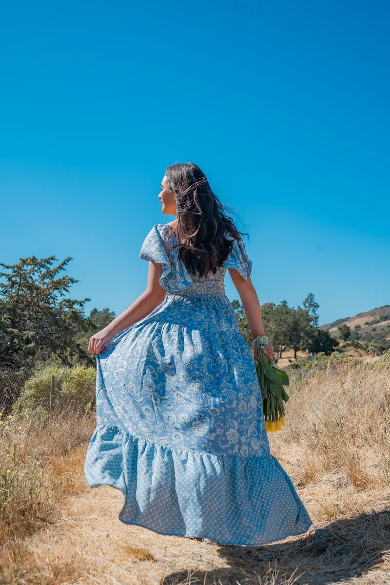 A woman in a long blue dress walking through golden grass