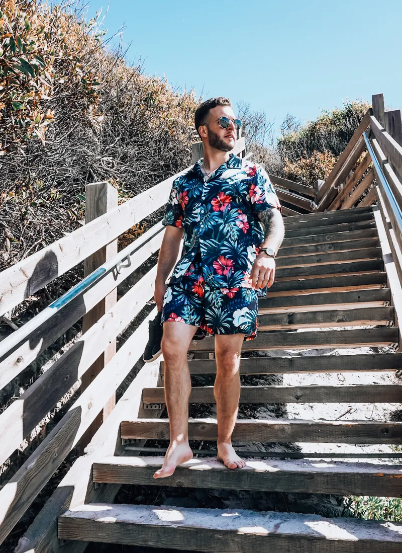 A man in a floral shirt and shorts walking down wooden beach stairs