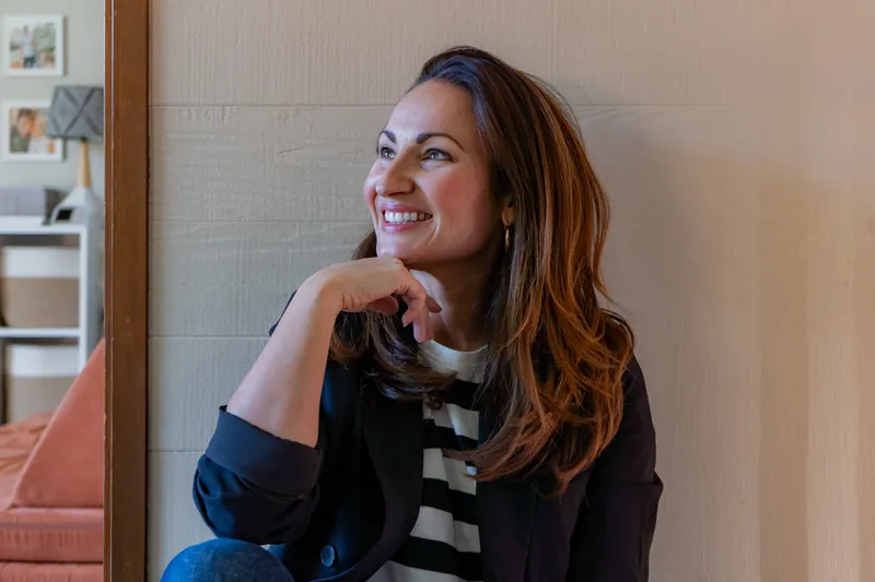 A business owner smiling by a doorway in a blazer and striped top
