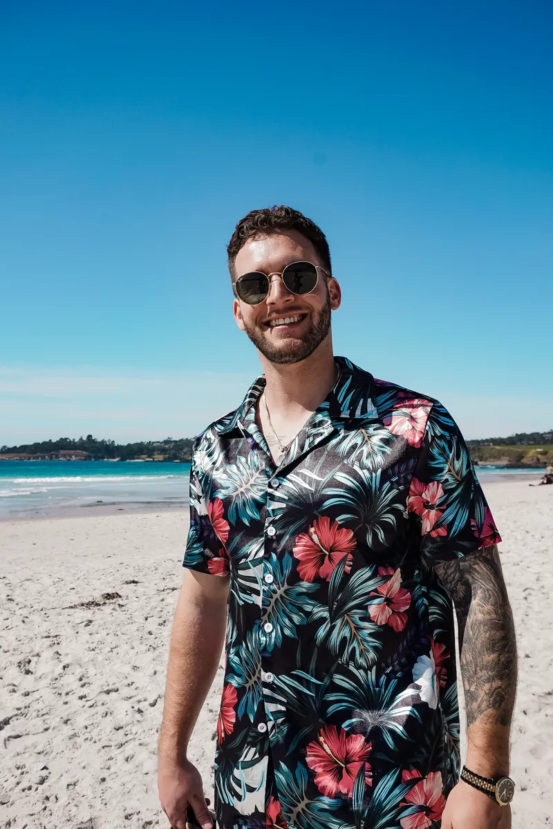 A man smiling on the beach in a floral shirt