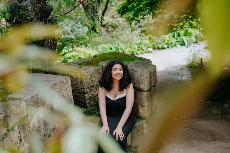 A senior seated on a mossy stone wall, framed by leaves