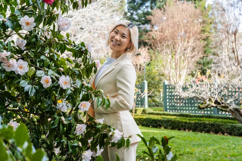 Smiling beside a camellia bush in a cream suit