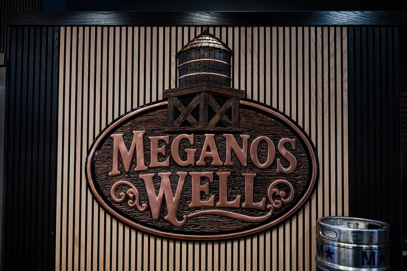 The carved Meganos Well sign, with a water tower on top, on a slatted wood wall