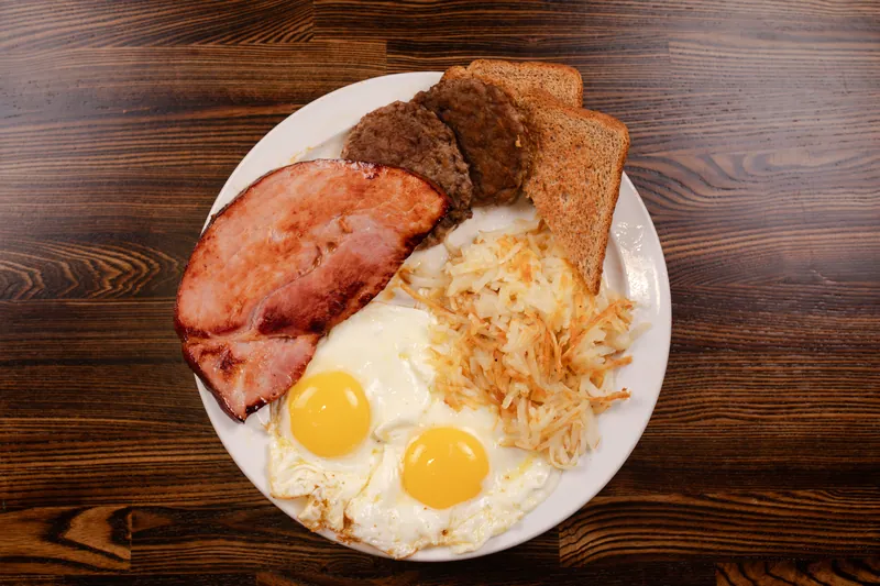 Ham steak, two sausage patties, two fried eggs, hash browns, and toast, from above
