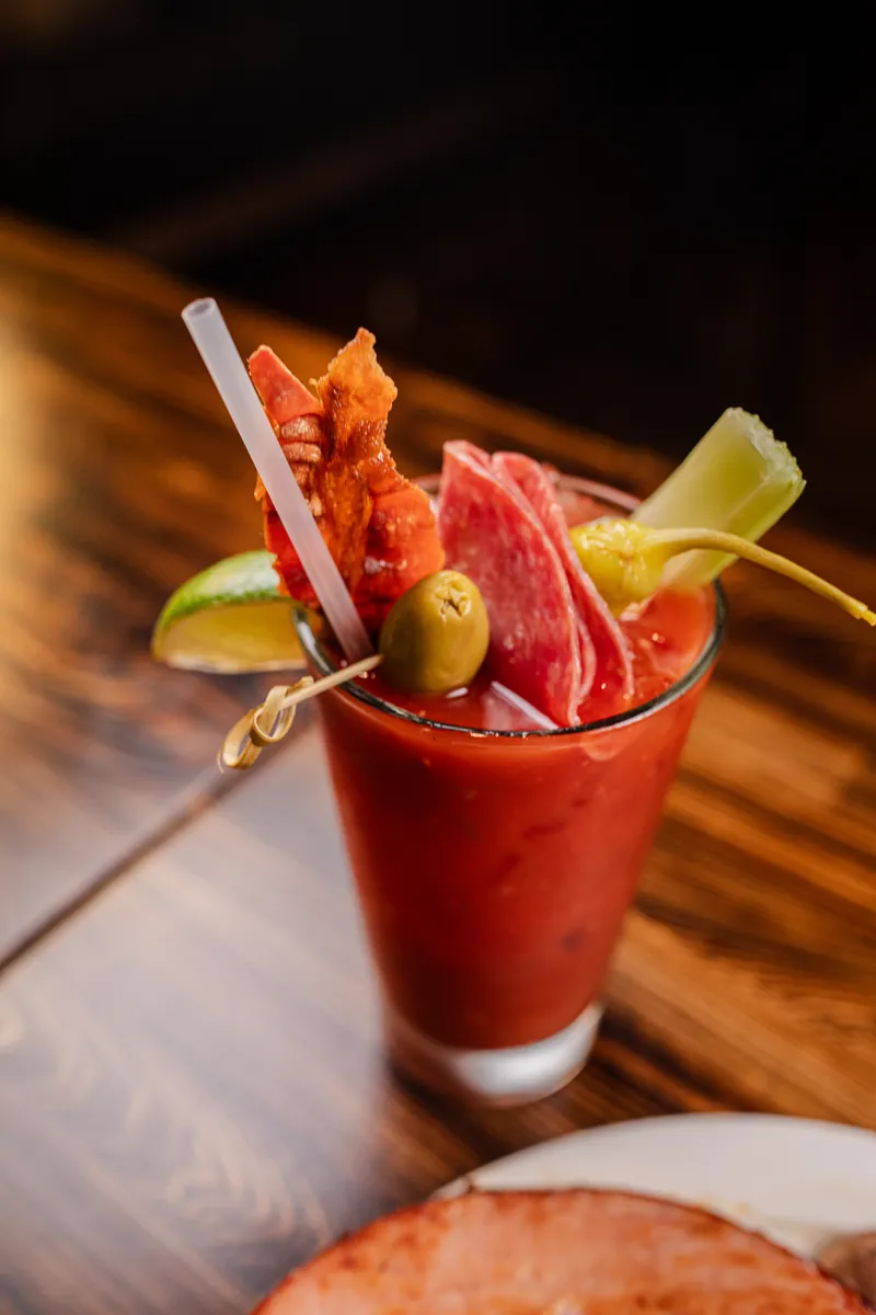 A Bloody Mary topped with salami, bacon, an olive, a pepperoncini, celery, and lime