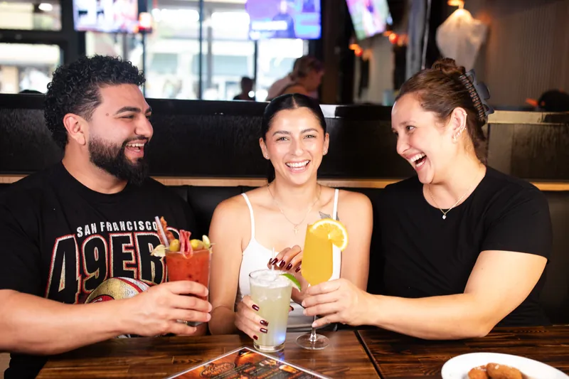 Three guests laughing and toasting with drinks in a booth