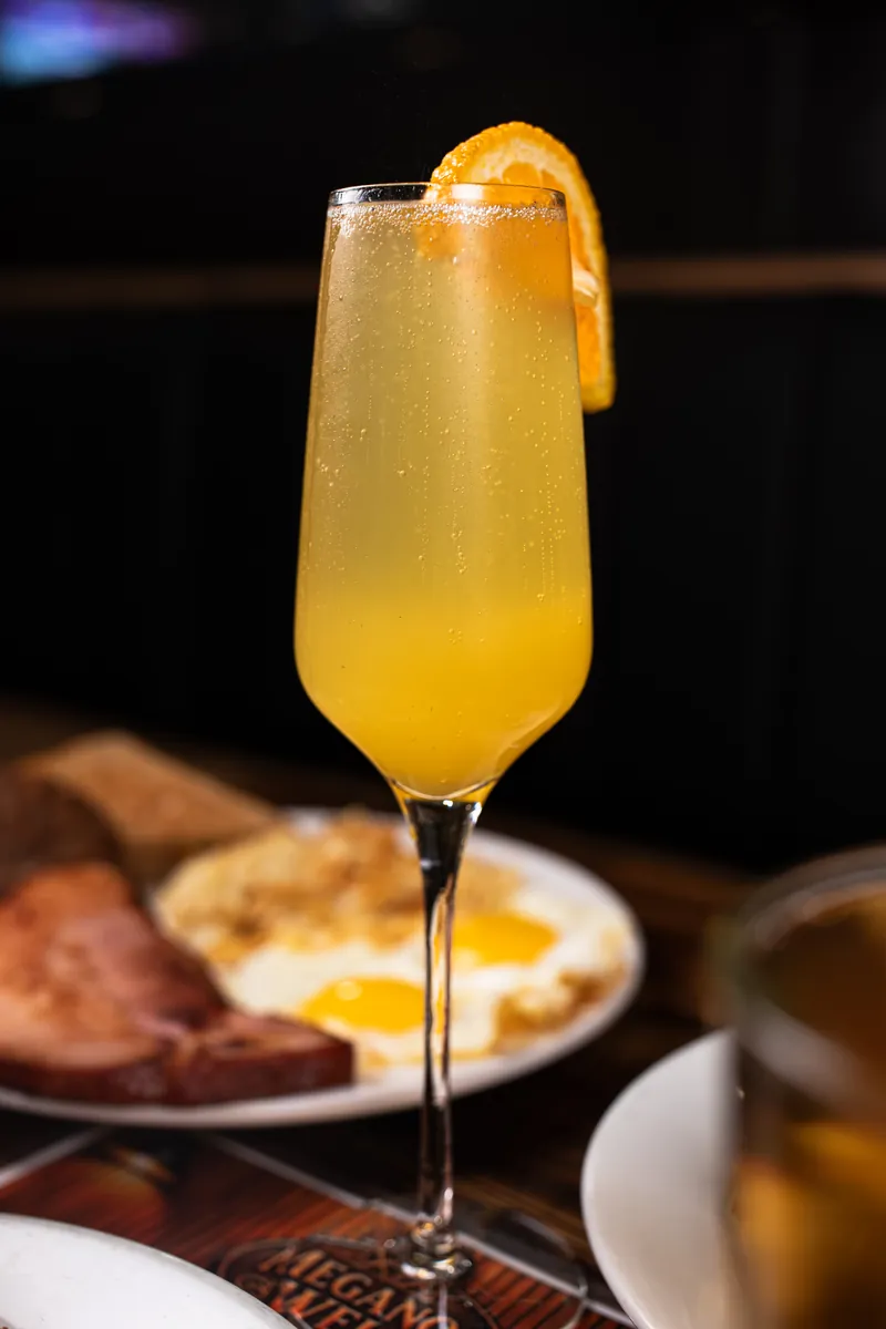A mimosa in a tall flute, with breakfast behind it
