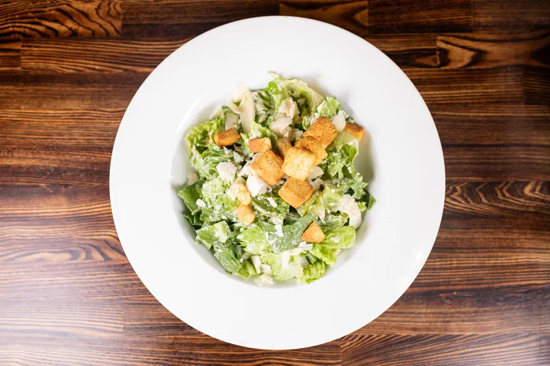 Romaine with croutons and shaved parmesan in a white bowl, from above