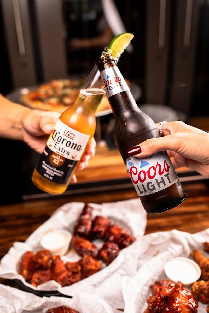 Two beers clinking over baskets of wings