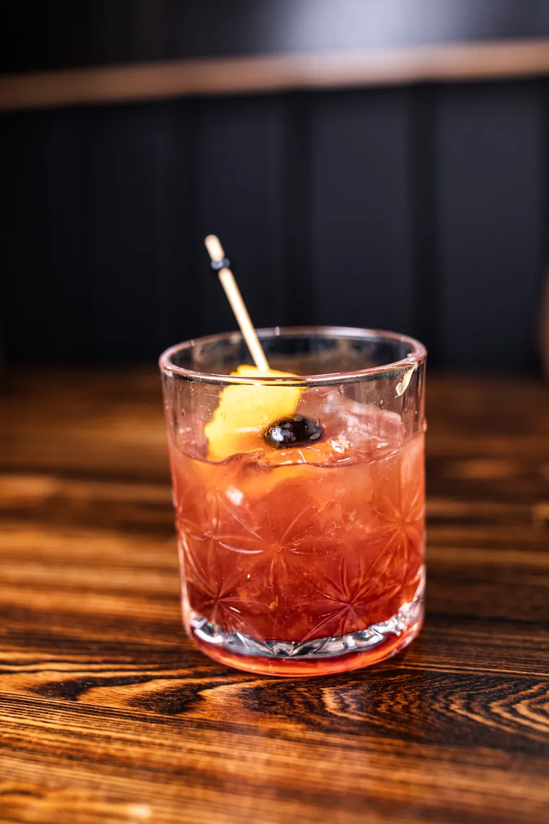 A red drink on the rocks with a cherry and an orange peel