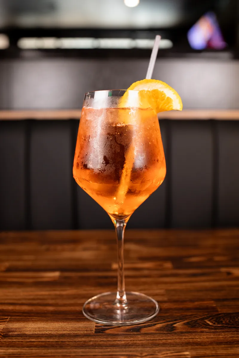 An orange drink over ice in a wine glass, with an orange slice