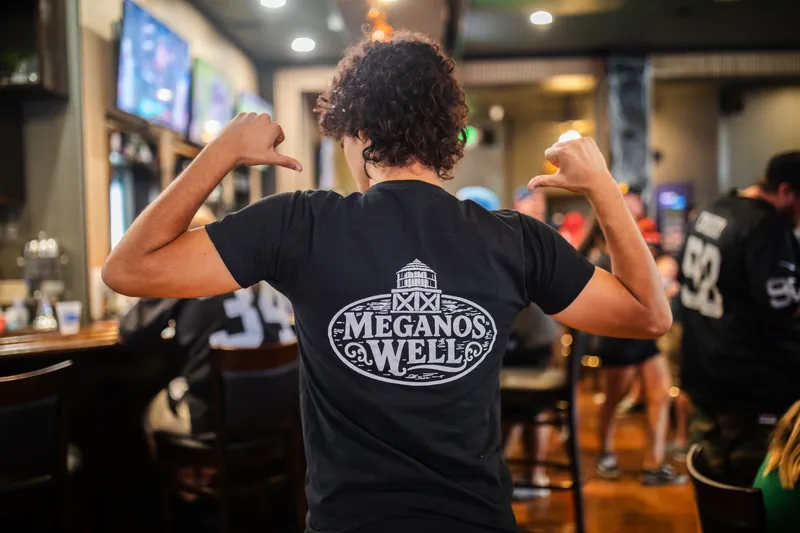 A staff member pointing to the Meganos Well logo on the back of his shirt