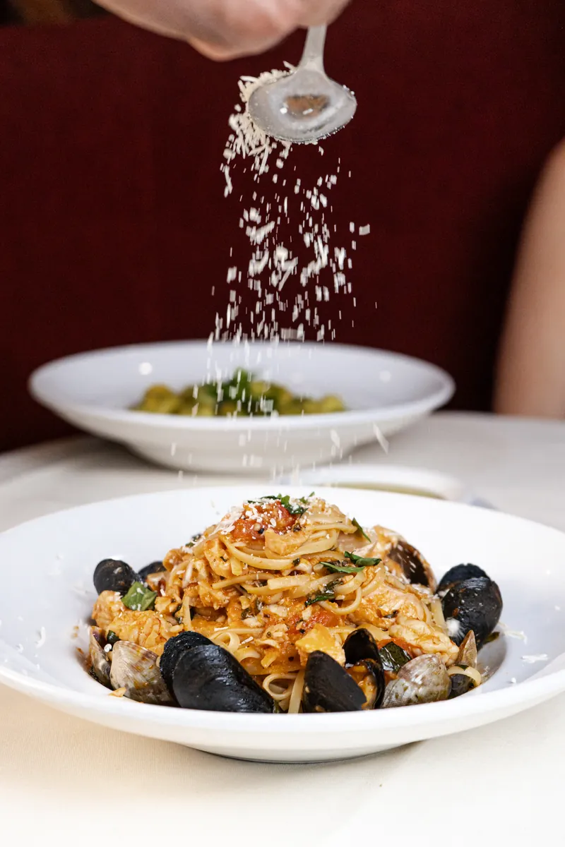 Parmesan falling onto a plate of seafood pasta