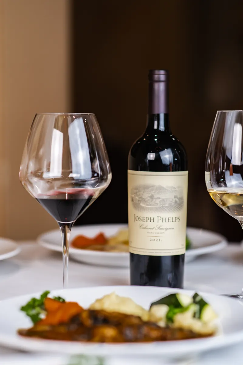 A bottle of red wine and two glasses beside a plated entree