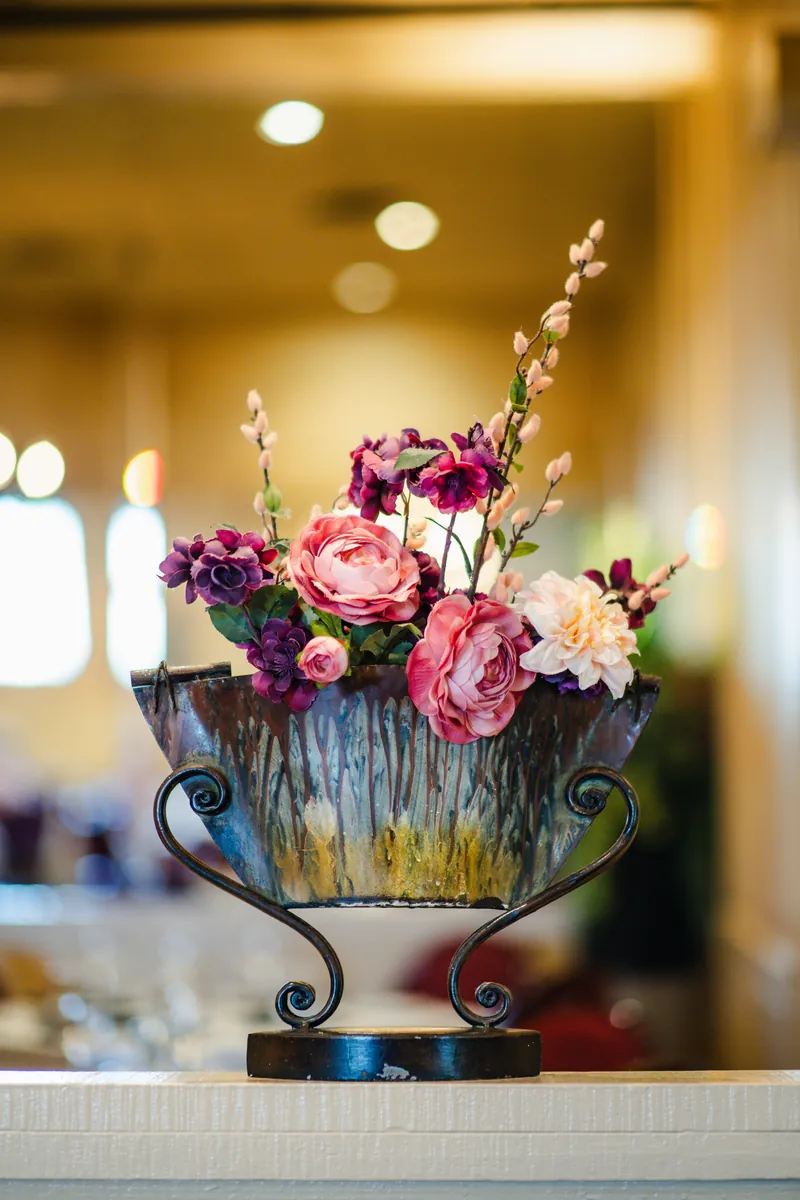 Pink and purple flowers in a metal urn, the dining room glowing behind