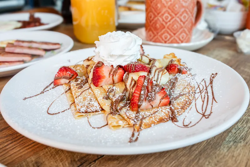 Crepes with strawberries, banana, chocolate drizzle, and whipped cream