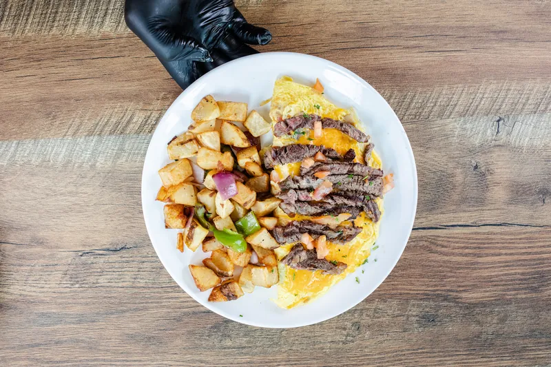 A gloved hand sets down a steak omelette with home fries