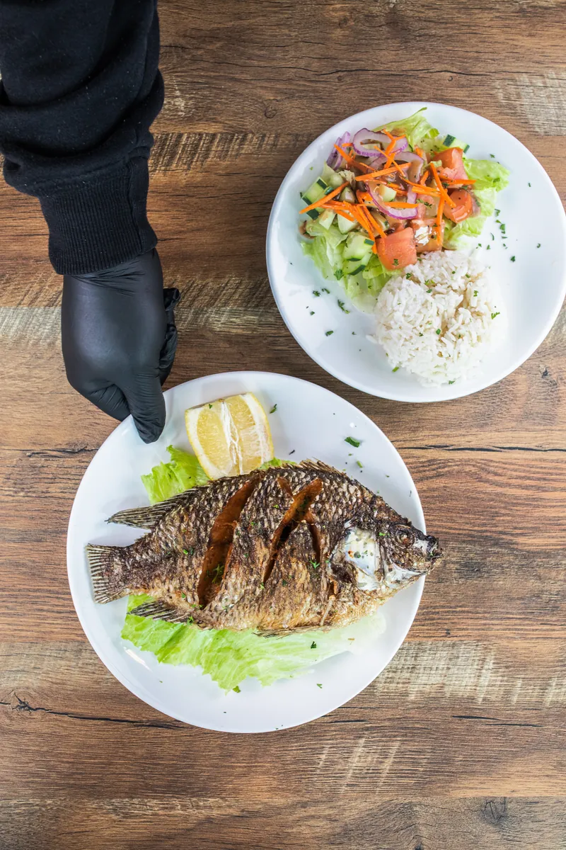 A gloved hand serves a plate of fried fish