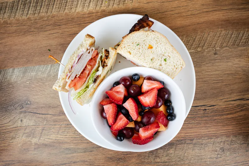 A club sandwich with a bowl of berries and cherries